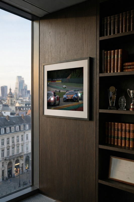 Framed picture of a race car on a wall next to a bookshelf with books and awards in an office, perfect for decoration.